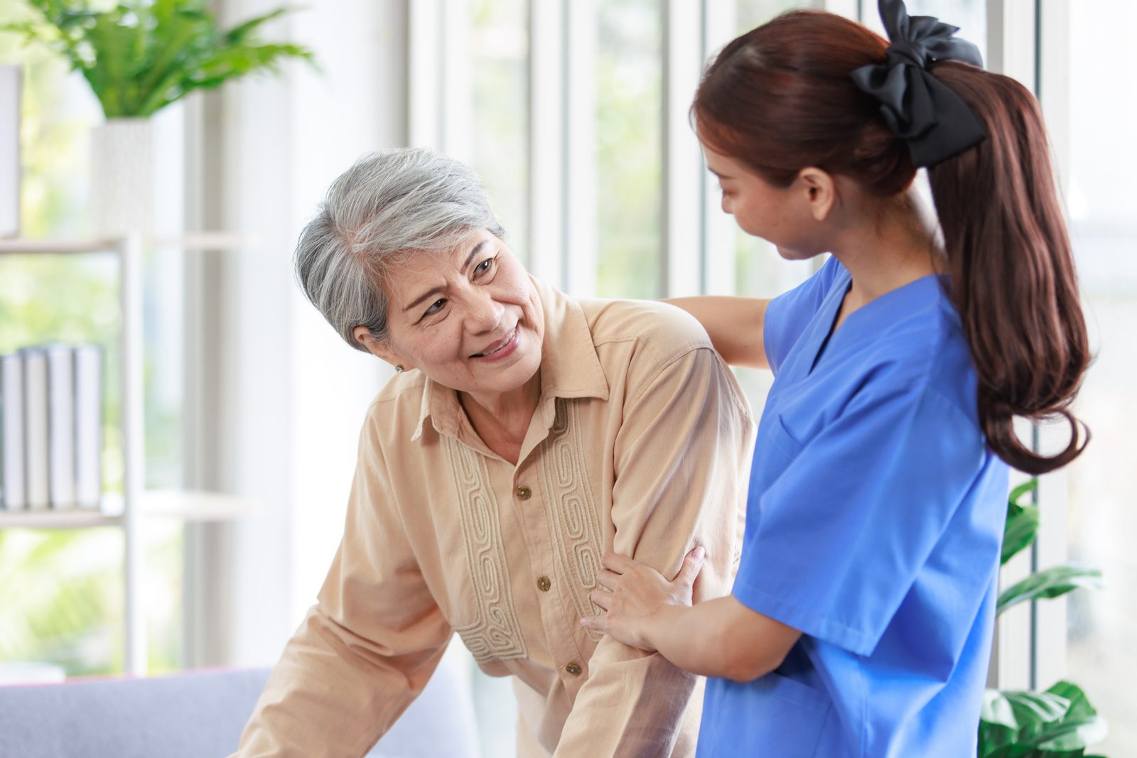 A caregiver steadying a smiling senior woman as she walks across her living room