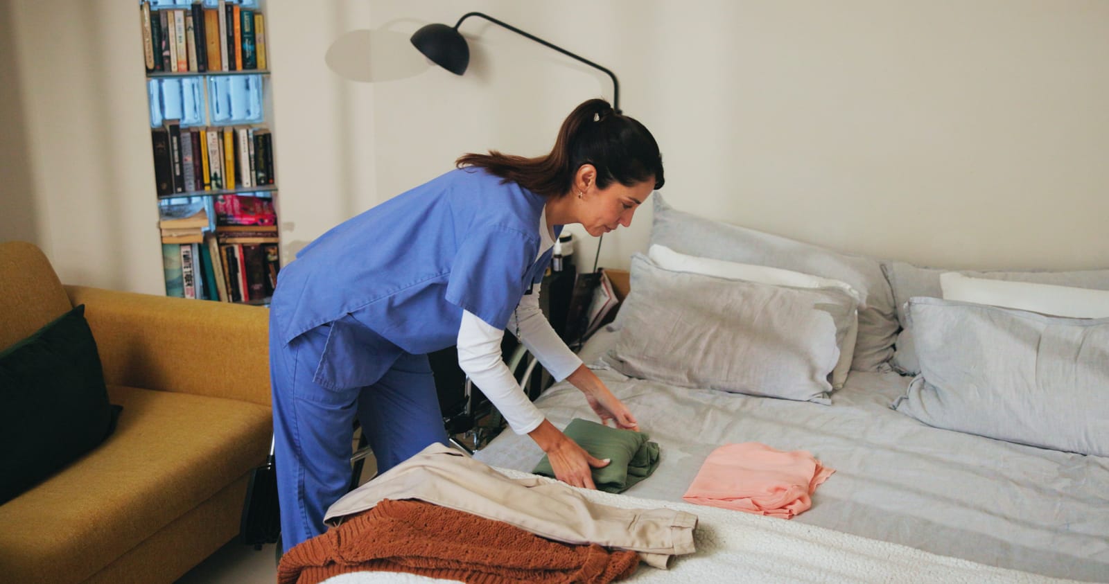 A home care worker preparing a clean, comfortable bed in a client's home