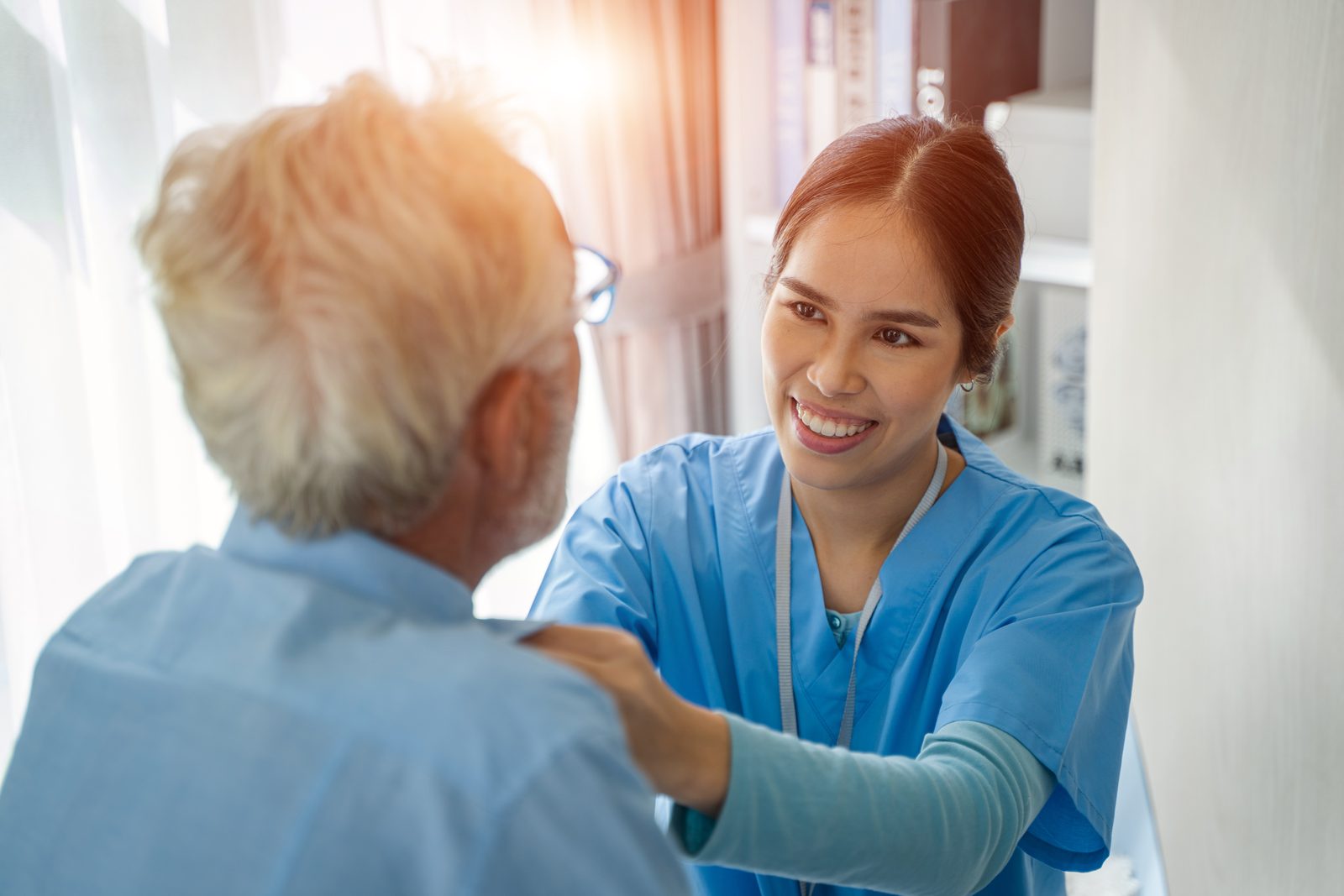 A smiling home care worker reassuring a senior man with a hand on his shoulder