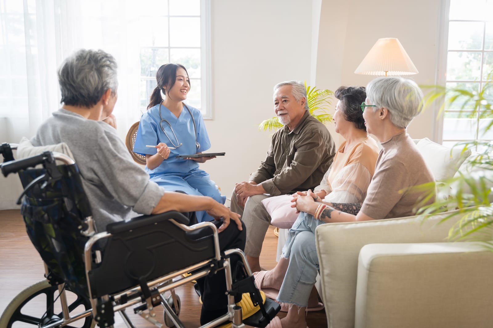 A nurse with a tablet leading a group care session with residents in a care setting