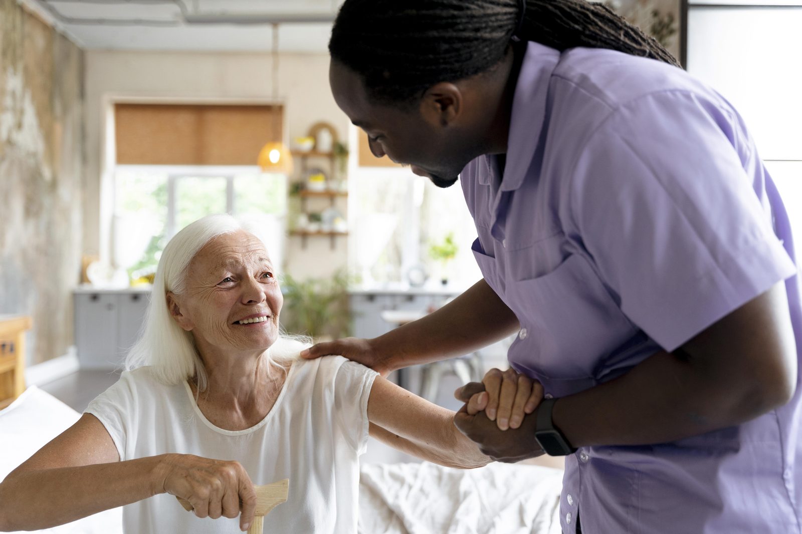 A home care worker gently helping a smiling senior woman stand up at home